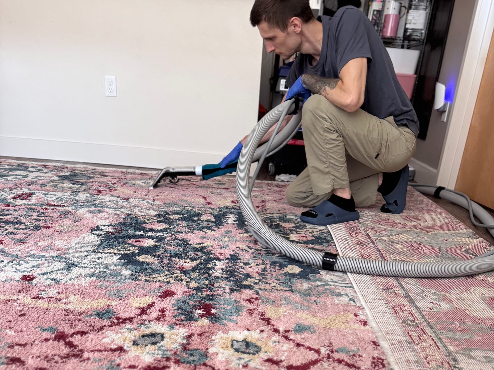 MagiClean technician cleaning a pink and blue patterned area rug in a Seattle home with a hand extraction tool