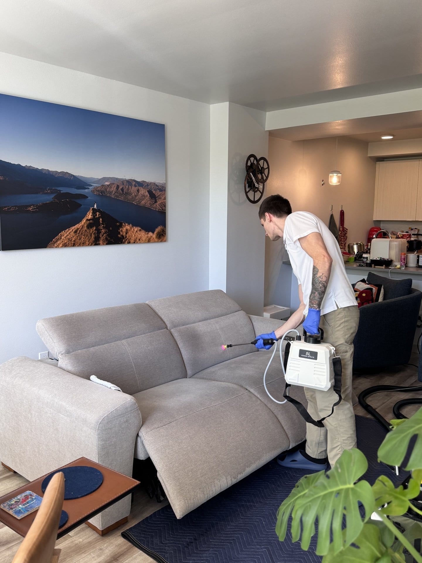 MagiClean technician applying fabric-safe pre-treatment to a beige reclining sofa with a pump sprayer